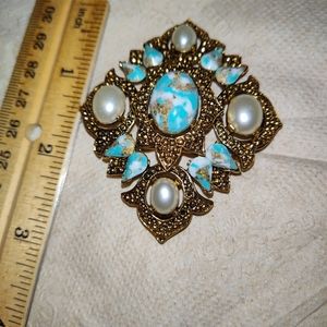 A gold tone brooch faux pearl, blue, gold, and white color on the stones